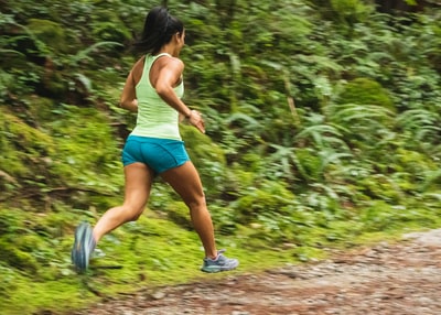 Woman wearing a white vest on a dirt road running during the day
